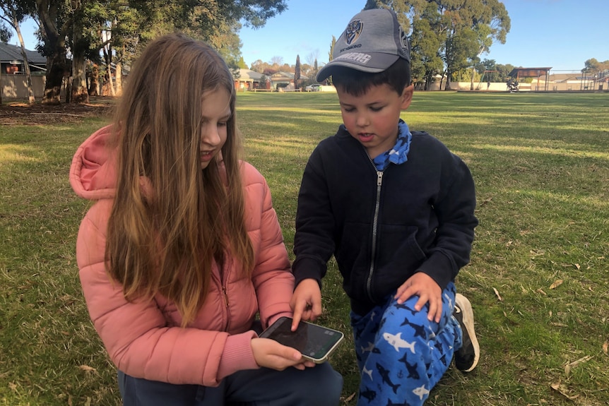 Girl and boy looking at a map on a smart phone in a park