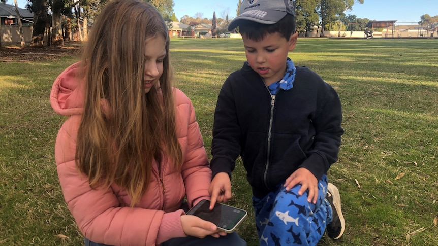 Girl and boy looking at a map on a smart phone in a park.