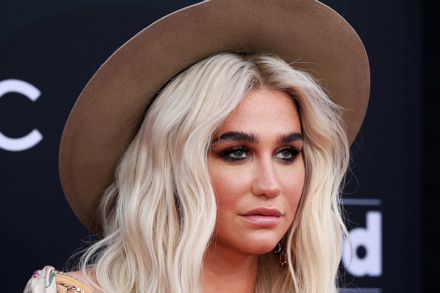Kesha wearing a brown, wide-brimmed hat with her blonde, wavy hair out.