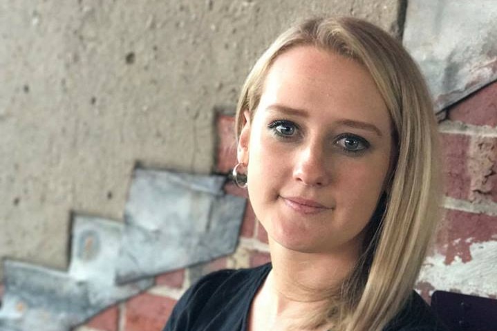 Caitlin Powell, a woman with blonde hair and a black top, smiles at the camera.