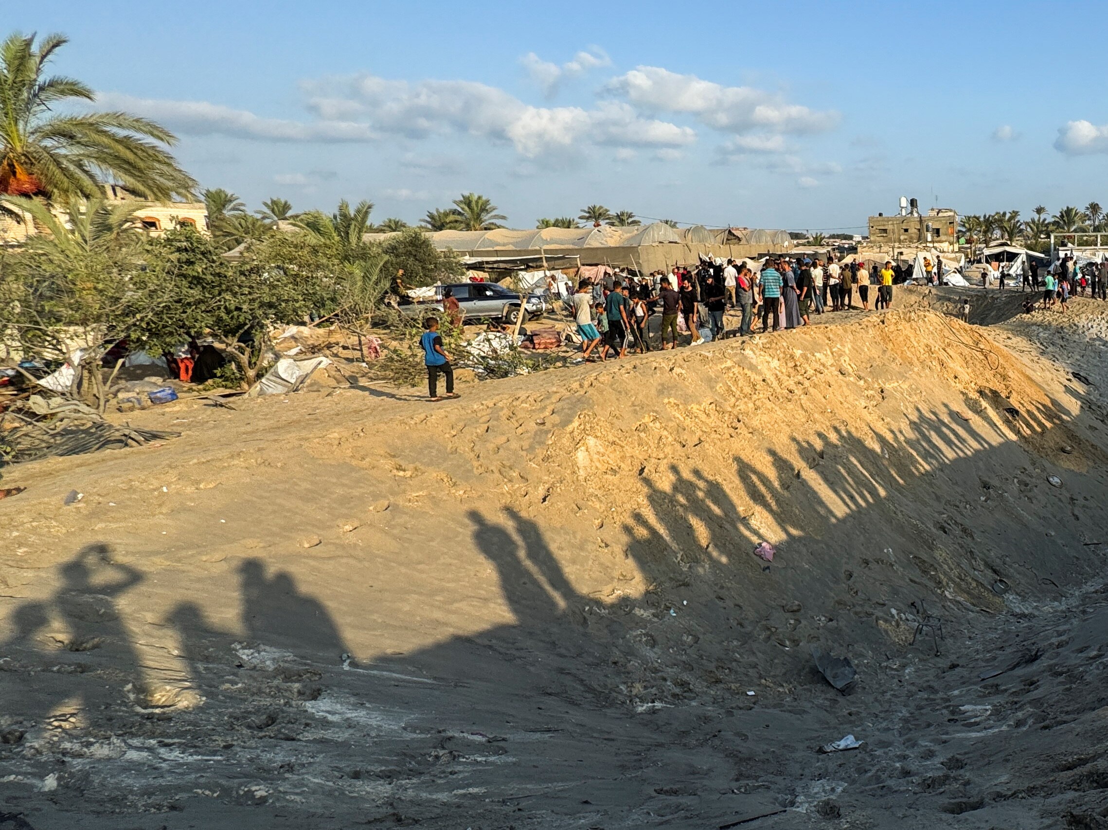 A group pf people look at a large crater in the sand