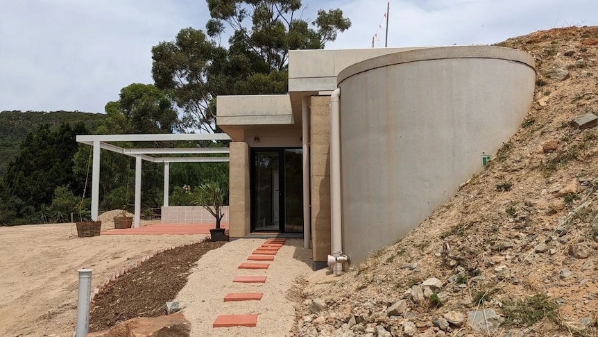 A concrete house and water tank built into the side of a dirt hill.