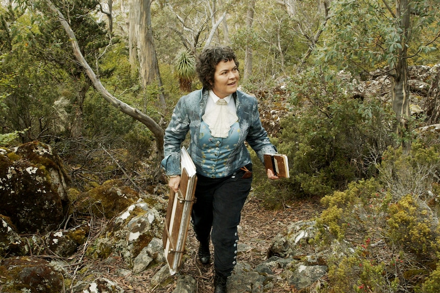 A woman in historical costume walks through a Tasmanian rainforest.