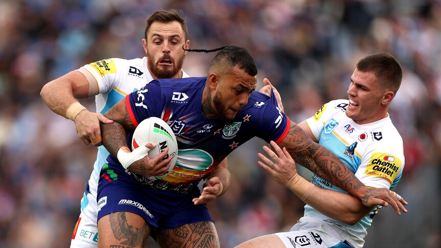 NRL player Addin Fonua-Blake running with the ball, trying to break the tackle of two defenders