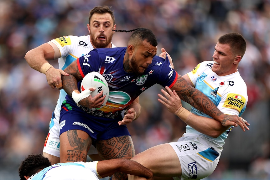 NRL player Addin Fonua-Blake running with the ball, trying to break the tackle of two defenders