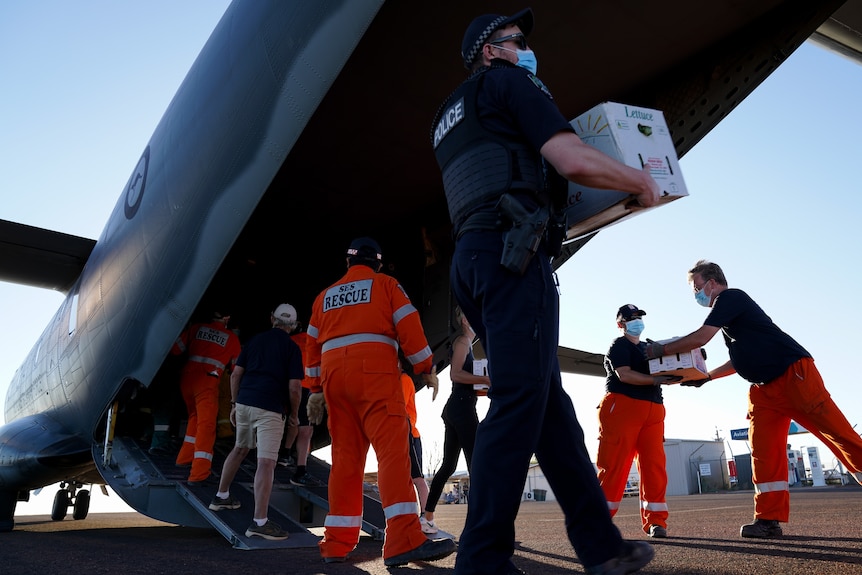 SES volunteers and a police officer unload boxes of food off a landed plane