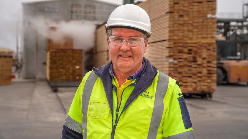 A man in a high vis, hardhat and safety glasses smiles for a photo.