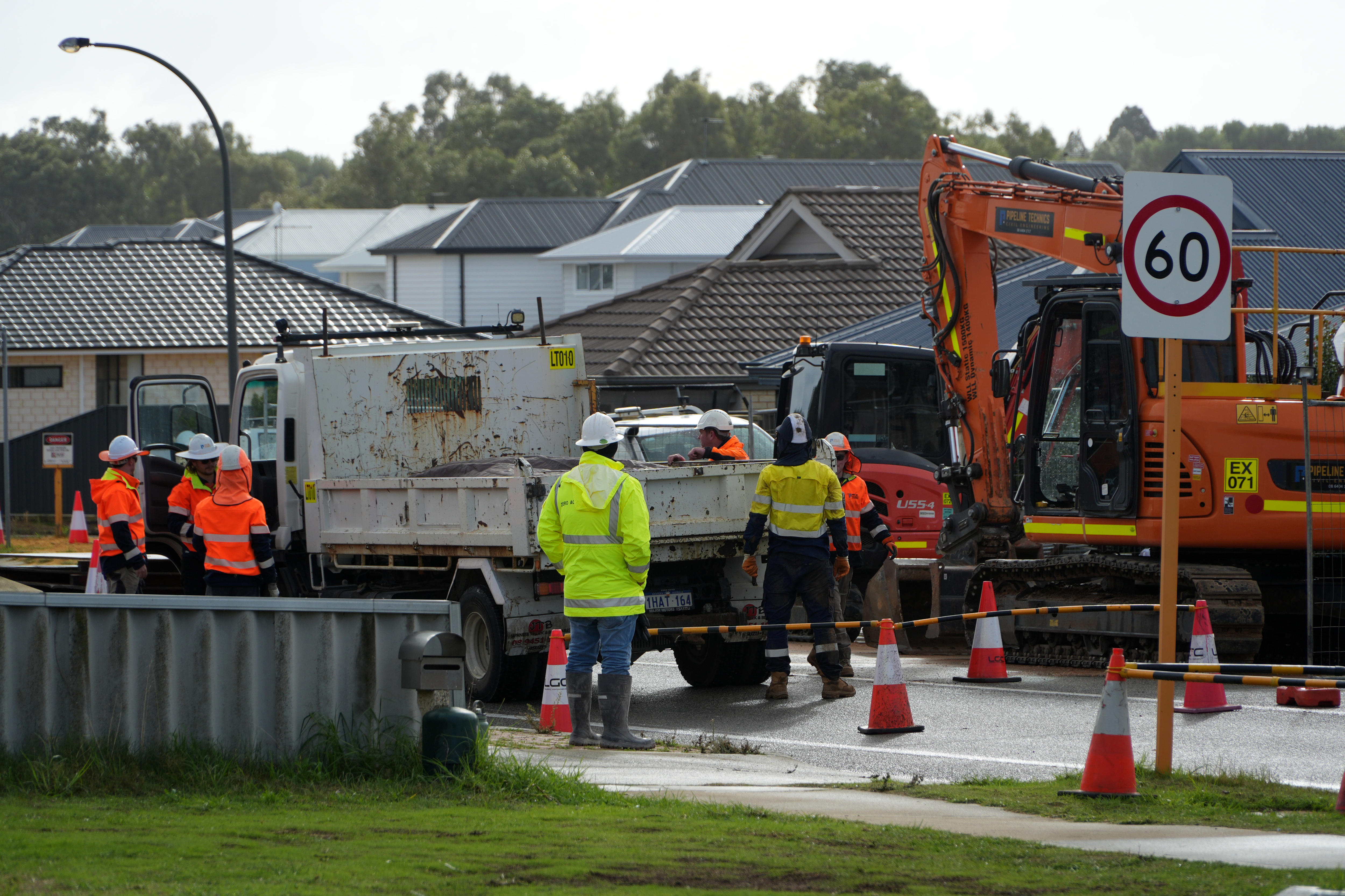Personal de emergencia en alta visualización en una calle suburbana con maquinaria pesada.