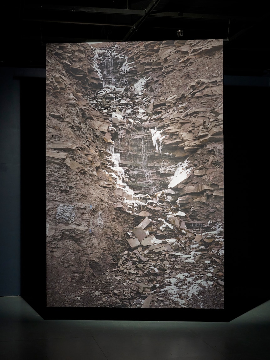A photograph of collapsed arctic terrain printed on fabric, displayed lit up against a dark background.