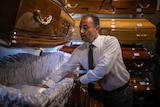 A man wearing a suit examines the satin interior of a coffin on display.