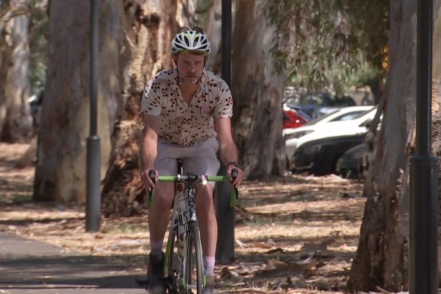 A man wearing a multi-coloured shirt riding a bike among trees