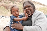 Indigenous woman and baby smiling at the camera in front of east macdonnell ranges 