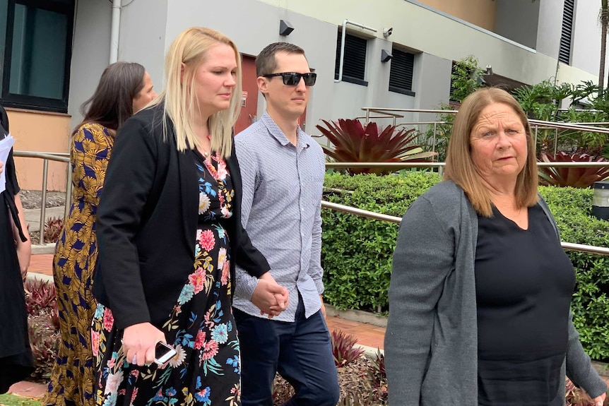 group of people walk young woman in floral dress with blonde hair holds hand of man woman in black shirt leads group