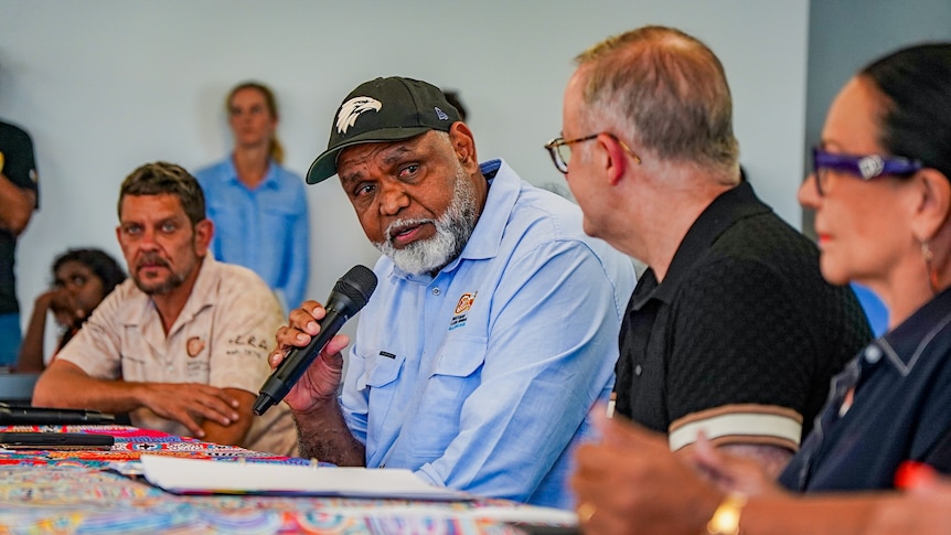 an Indigenous man with a microphone speaking to another man. 