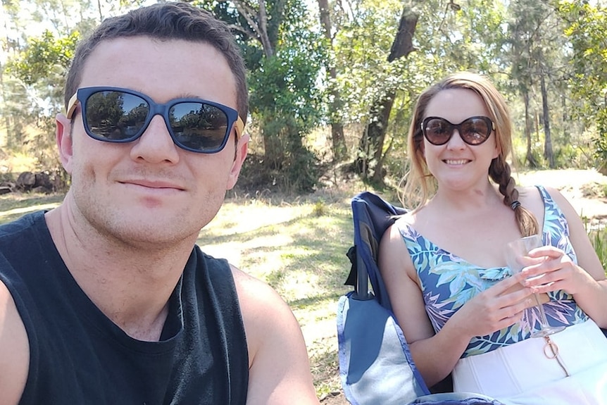 A man and woman wearing sunglasses and summer clothes sitting on fold out chairs under trees