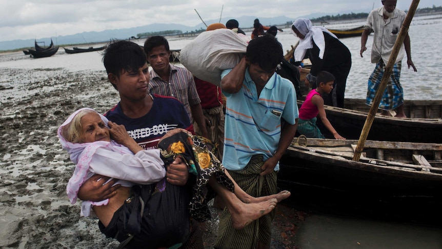 A Rohingya man carries an elderly woman from a boat