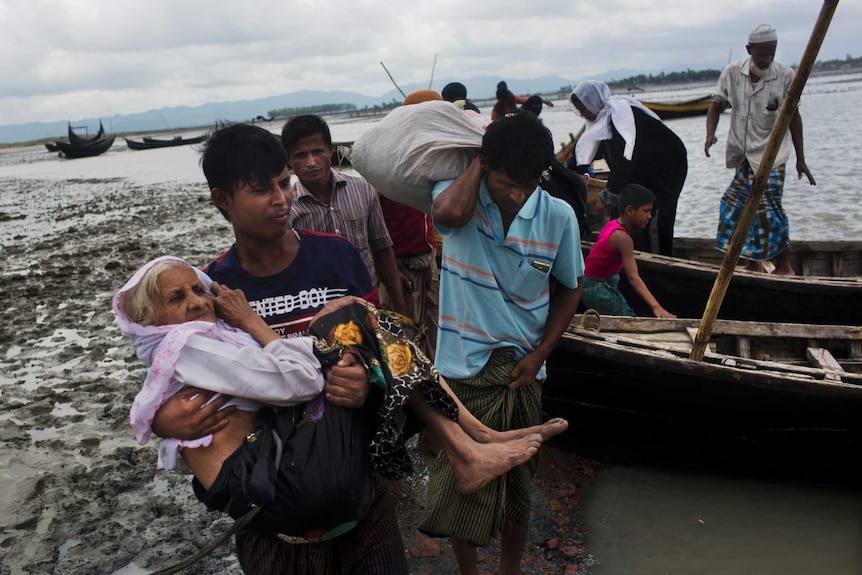 A Rohingya man carries an elderly woman from a boat