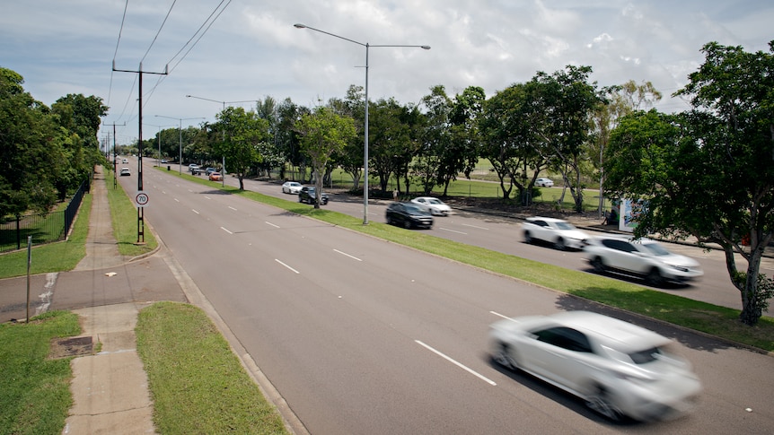 Cars travelling on a busy road, surrounded by grass and trees. 