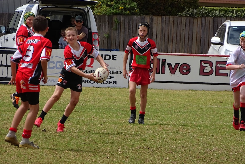 Young children play rugby league in red colours.