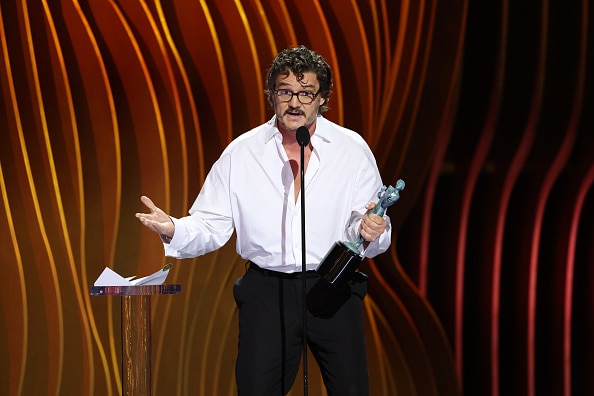 Pedro Pascal on stage in a white shirt holding an award.