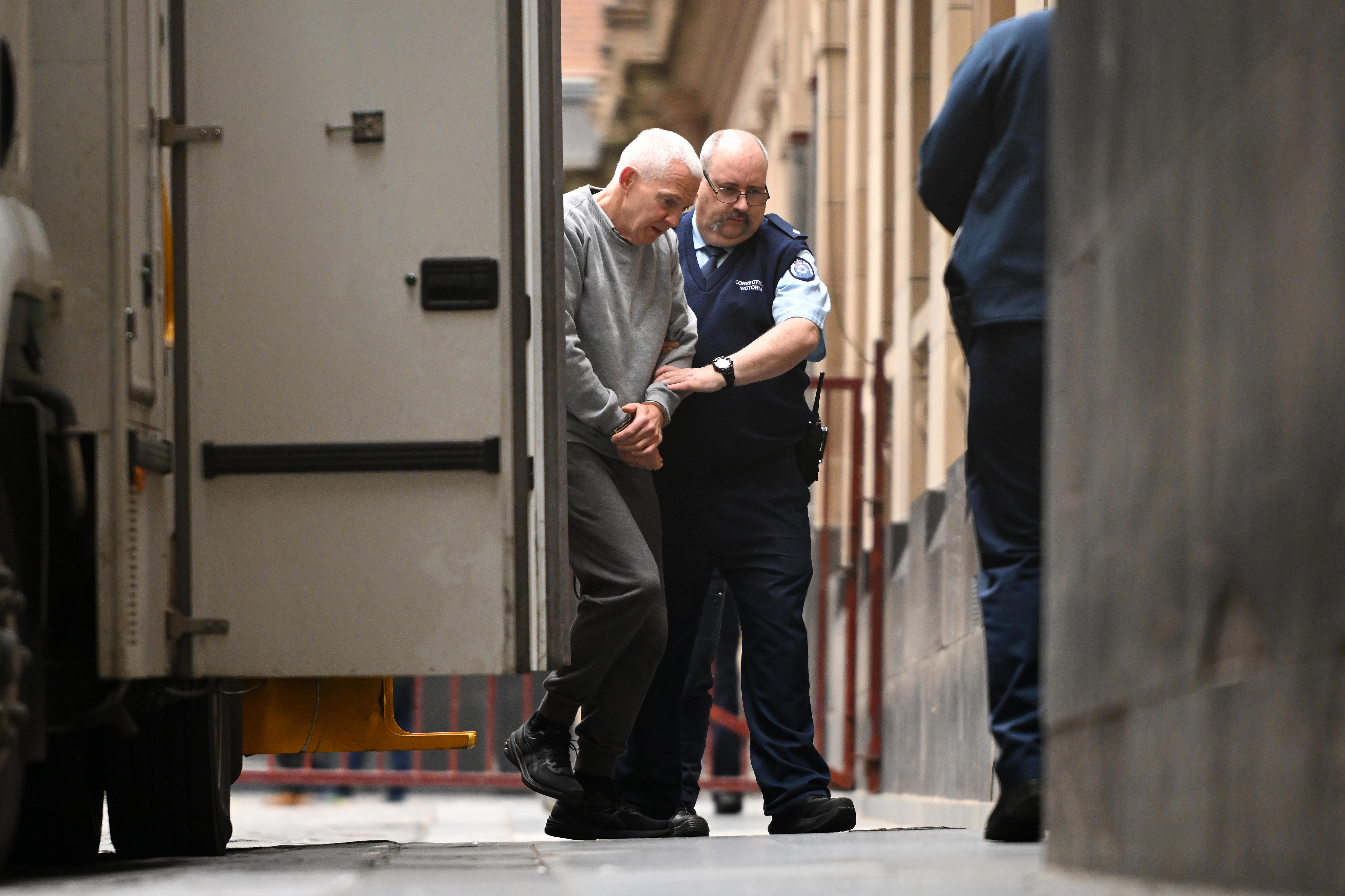 A man being led into a court building from a van in handcuffs.