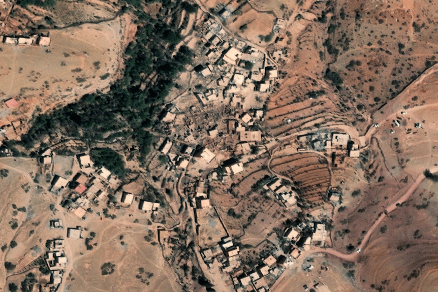 A birds' eye view shows the landscape of a village in a desert mountain region, several buildings destroyed