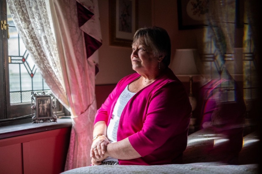 Val Stewart sits, looking out a window, her arms on her lap.