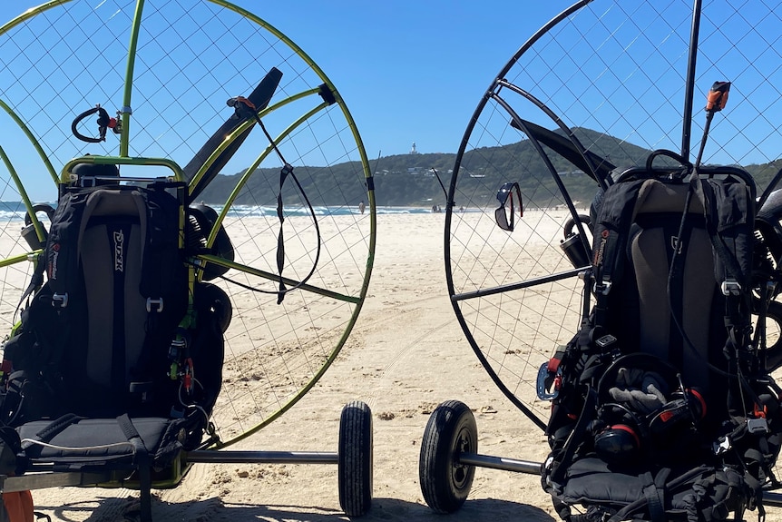 Two paramotors on a beach with a lighthouse in the distant background