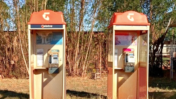 Two old style phone boxes covered in layers of red dirt.