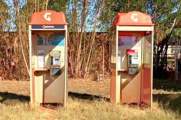 Two old style phone boxes covered in layers of red dirt.