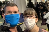 Selfie head shot of a man and a woman wearing face masks at an airport.