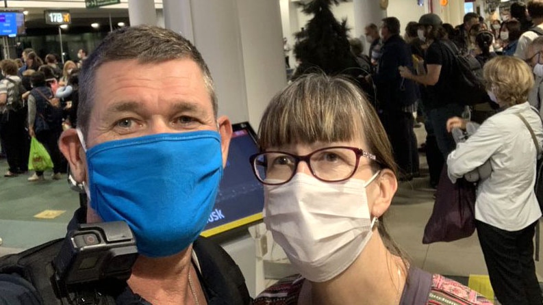 Selfie head shot of a man and a woman wearing face masks at an airport.