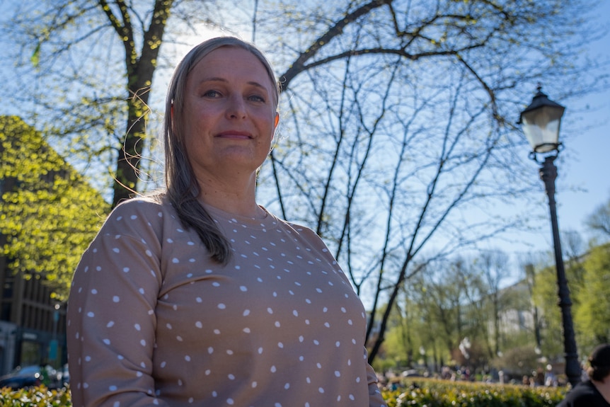 A woman with blond hair smiles while sitting on a bench in the park.