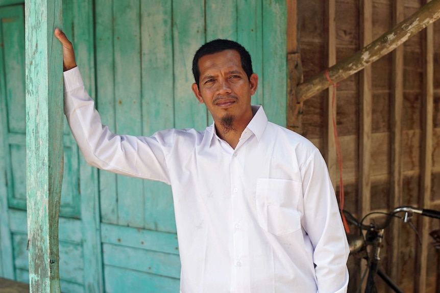 Sumarno, a recruit at the Peace Circle, stands beside a building leaning against a green wooden beam.