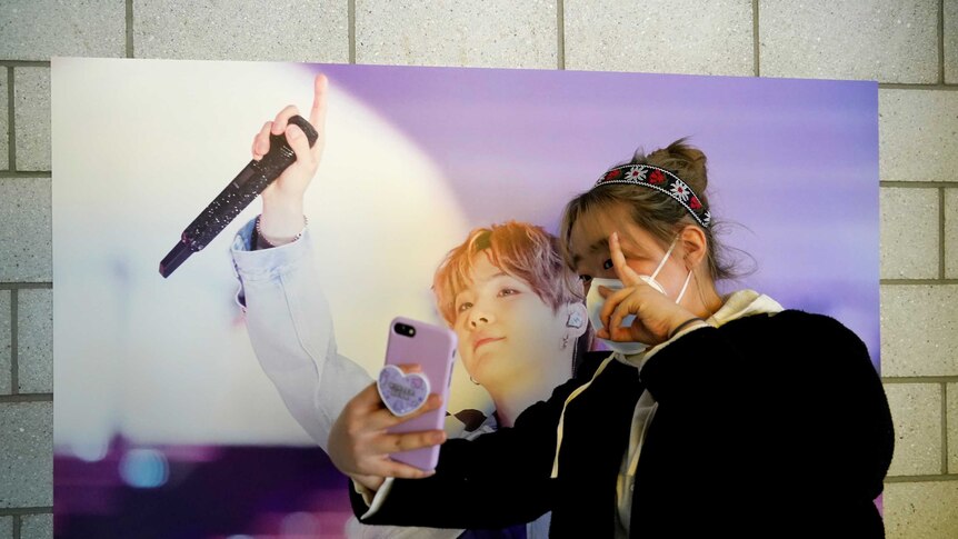 A fan of K-pop boy band BTS, takes a selfie while wearing a face mask at a cafe decorated with their merchandise.