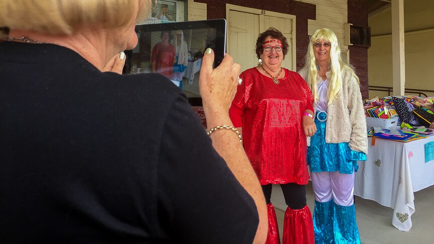 The back of a woman taking a picture on a tablet of two women in ABBA style costumes