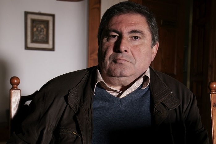 A man sits in a living room and looks at the camera as he poses for a photograph