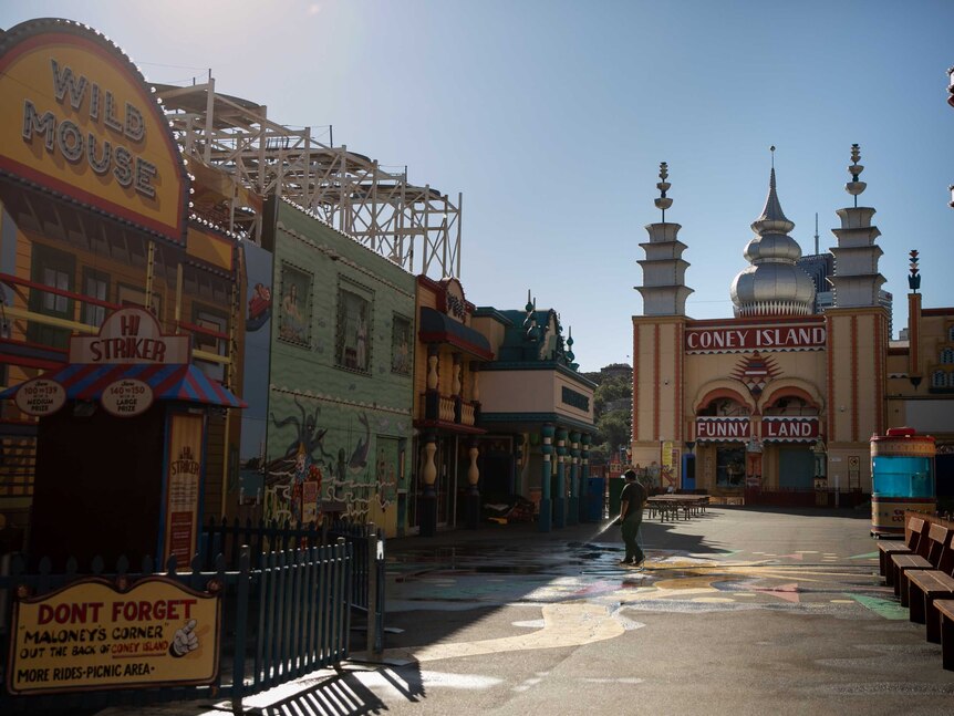 A cleaner hoses the pavement between the wild mouse and Coney Island attractions at Luna Park