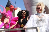 Three brightly dressed drag queens on a float.