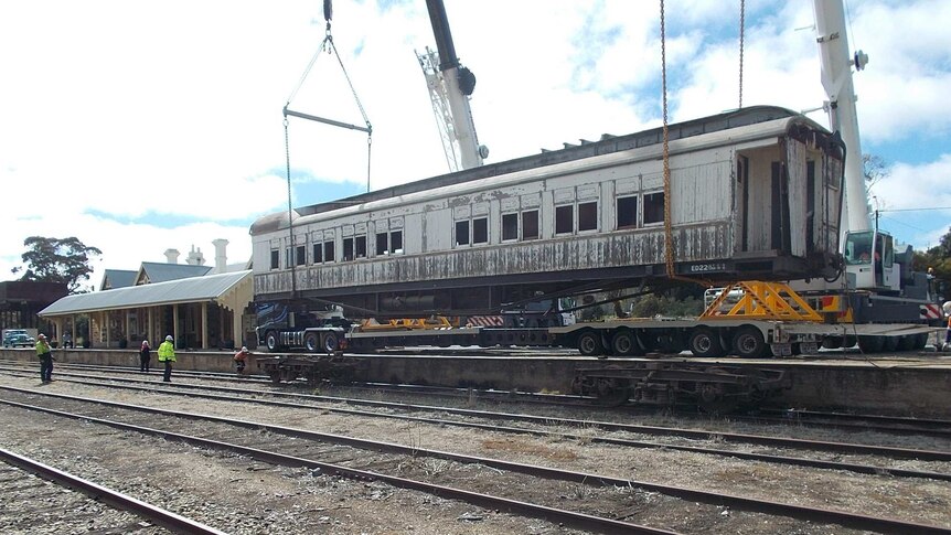 A large dining carriage is being lowered by cranes onto the train tracks.