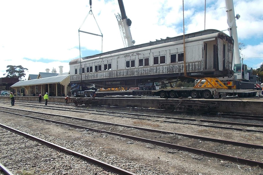 A large dining carriage is being lowered by cranes onto the train tracks.