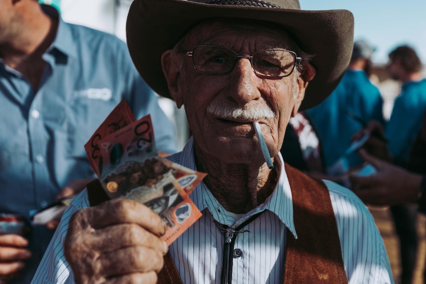 A man wearing a cowboy hat holding his winnings at a country race meeting.