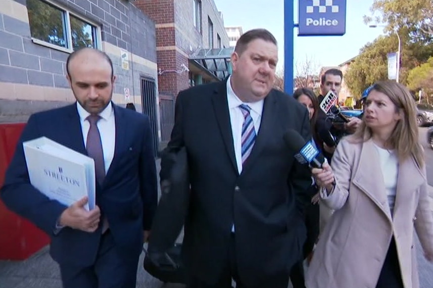 A man outside a police station talking to TV journalists.