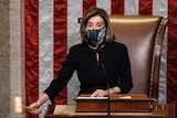 Nancy Pelosi, wearing a floral patterned mask, bangs a gavel on the desk in front of her