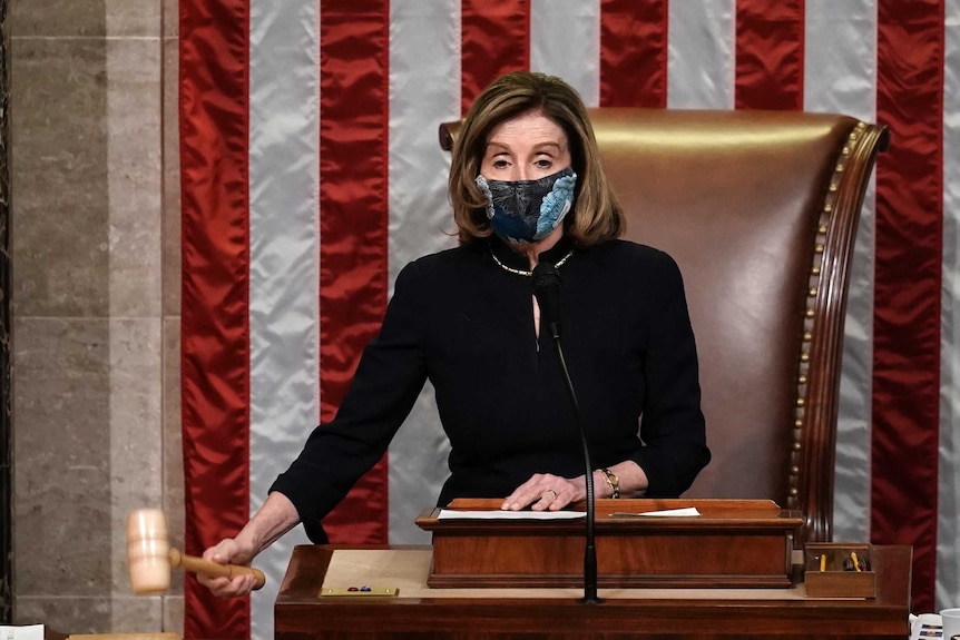 Nancy Pelosi, wearing a floral patterned mask, bangs a gavel on the desk in front of her
