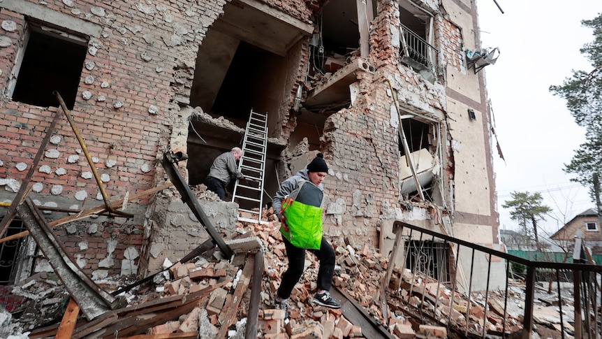 People carry belongings out of a residential building destroyed by recent shelling in Irpin.