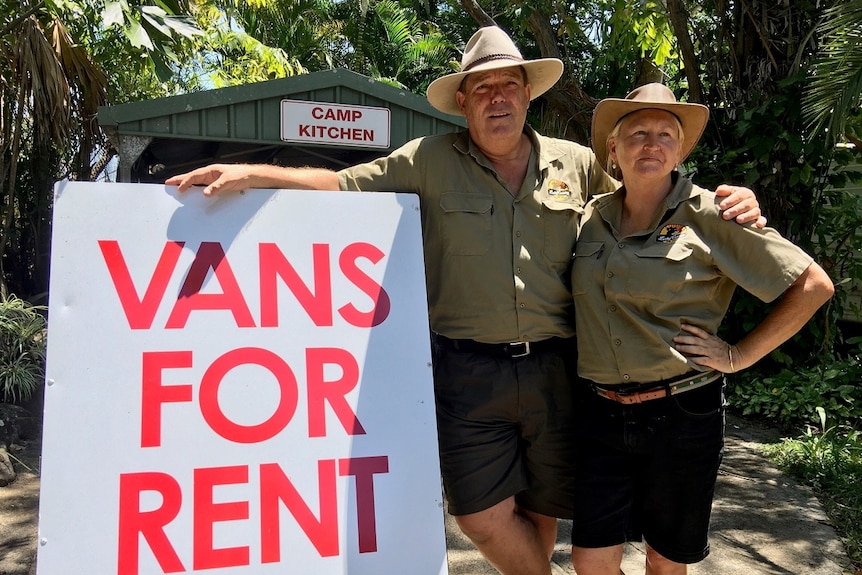 A husband and wife wearing khaki uniforms stand alongside a sign advertising vans for $200 a week