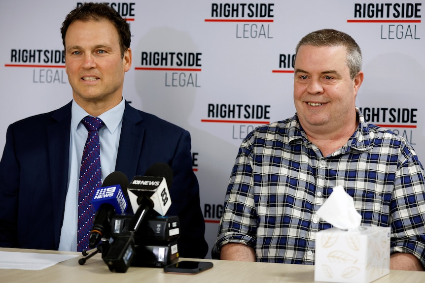 Michael Magazanik and Adam Kneale sitting at a table with microphones in front of them smiling.