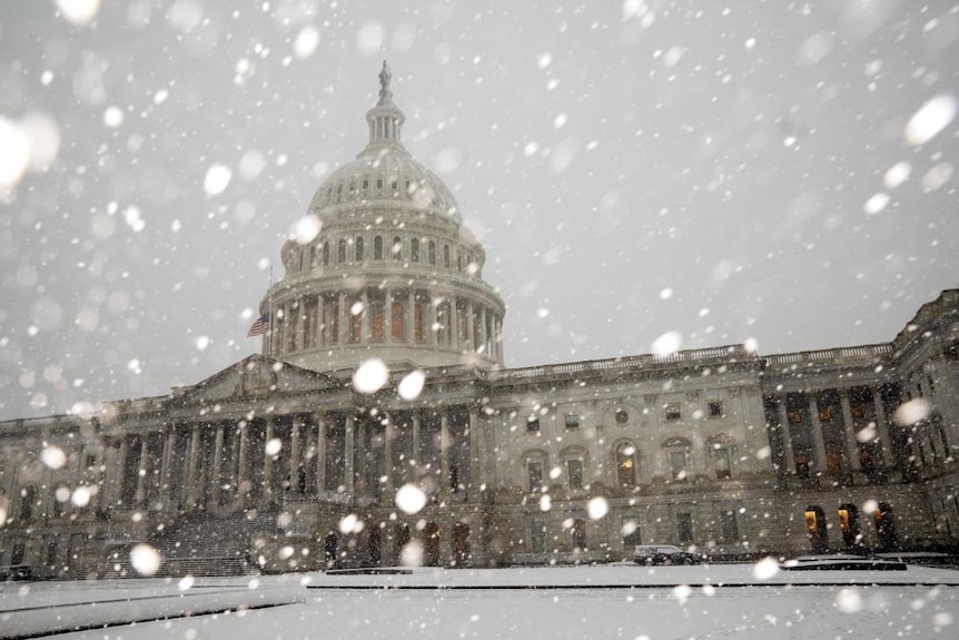 Drops of snow fall across the Capitol building in America amidst a gloomy grey sky day