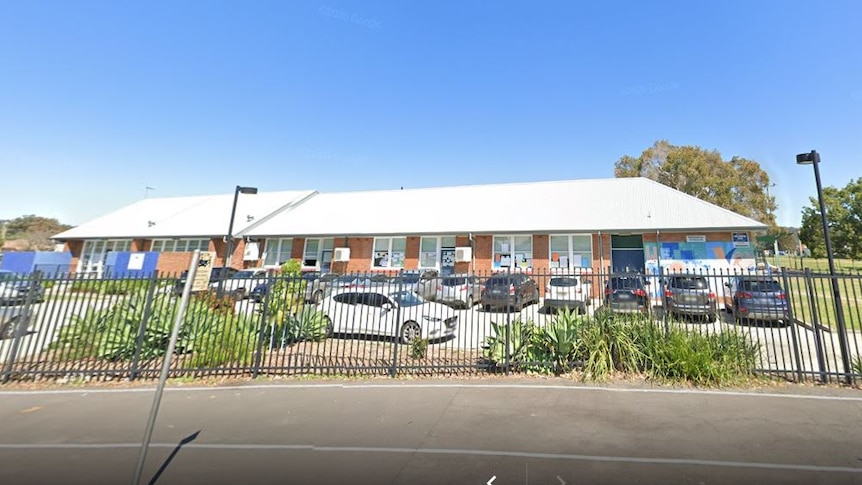 The exterior of a one-storey brick school with cars in the front